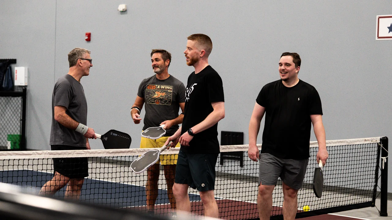 Four pickleball players gathered at the net with their paddles