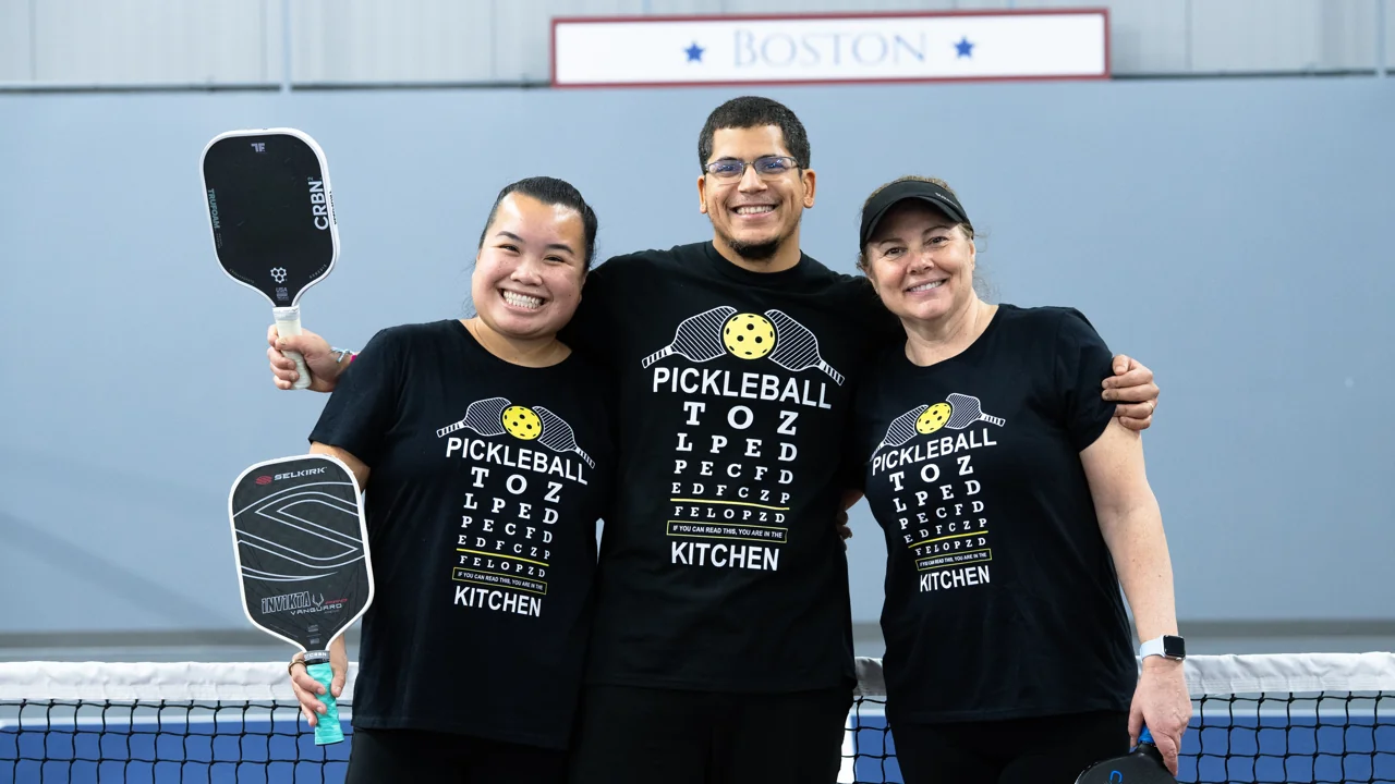 Three players in matching black pickleball shirts posing together on court